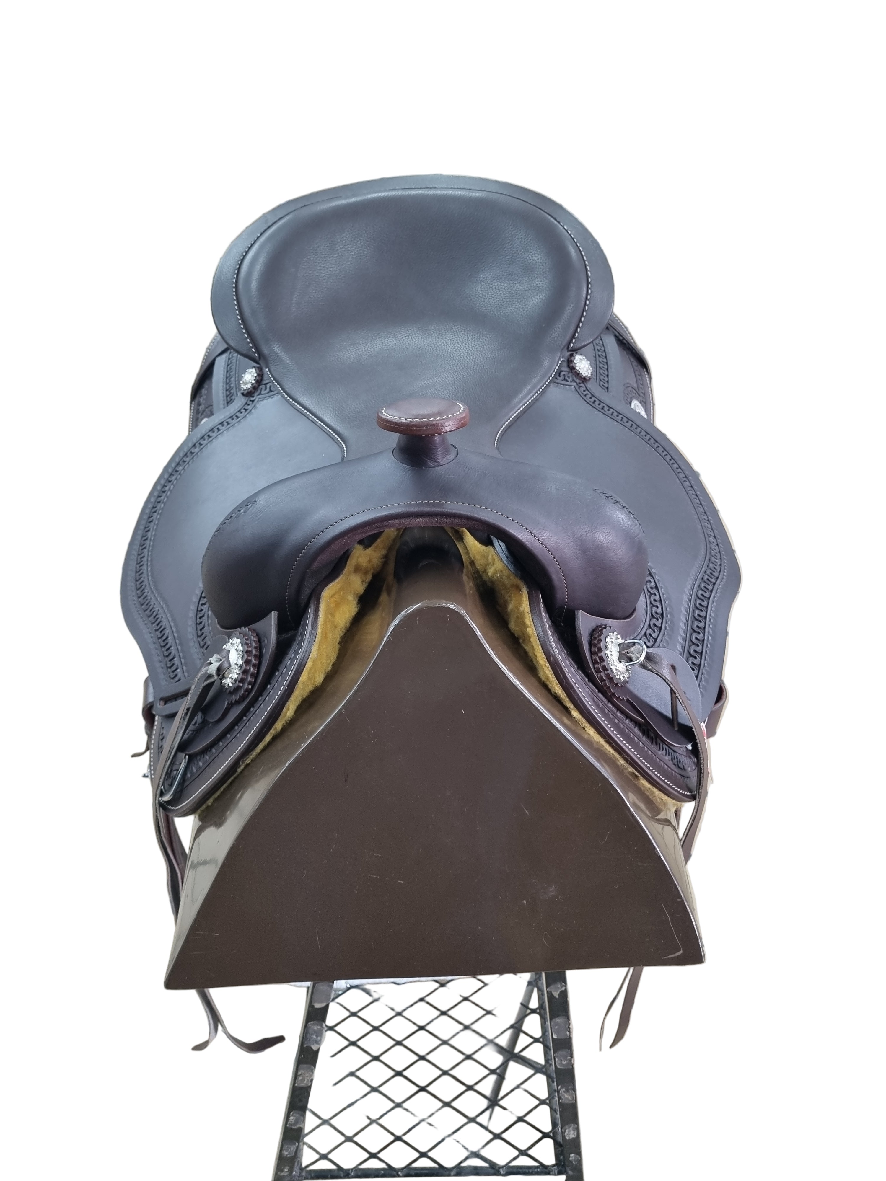 Brown leather saddle on a tiled floor with a metal gate in the background