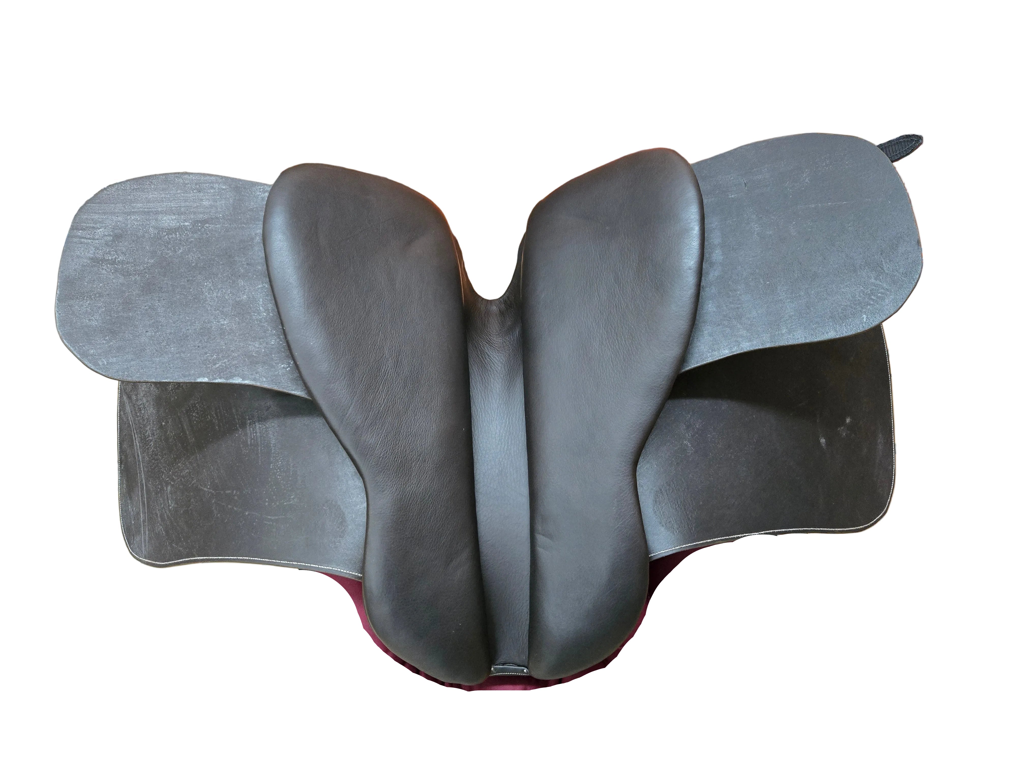 A black leather saddle pad with wing-like side wings, displayed on a chair with a burgundy cushion in what appears to be a workshop or storage room.